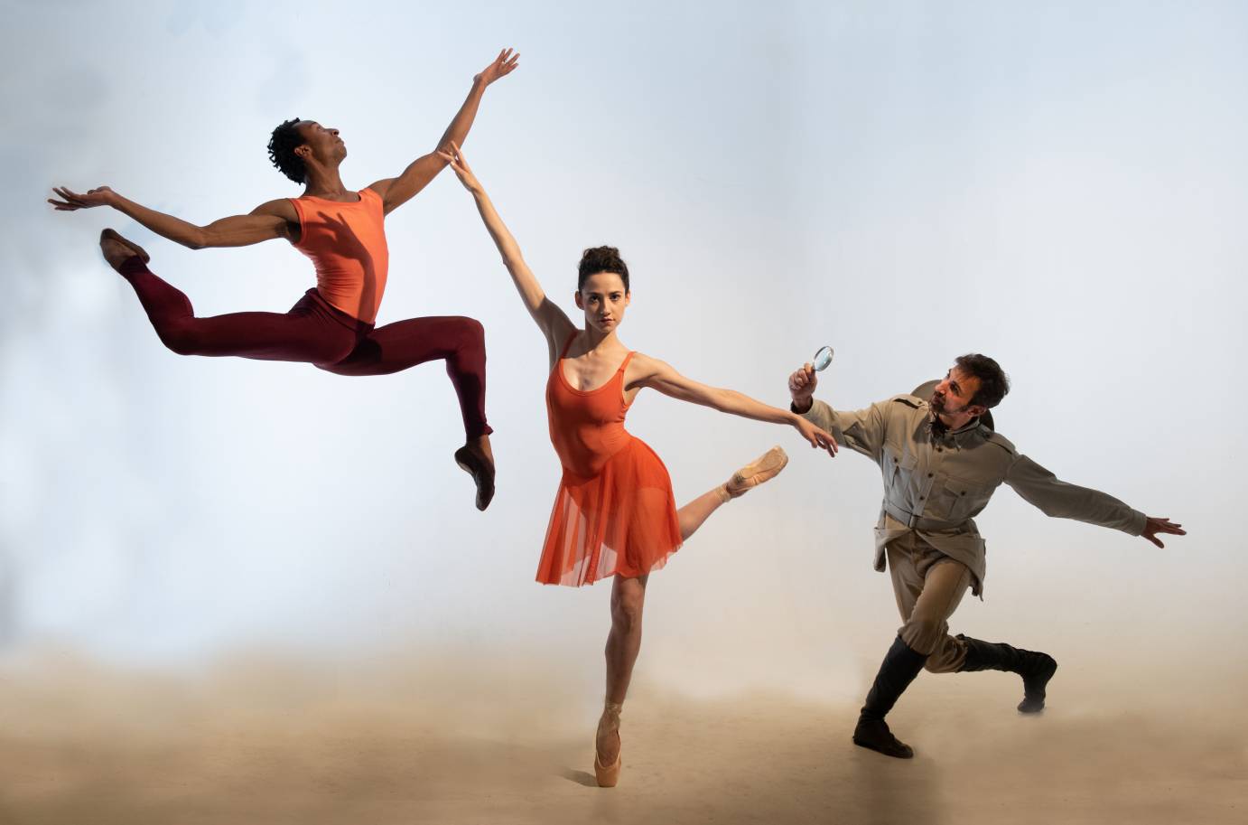 One dancer jumps into the air as one woman poses and a man holds a magnifying glass